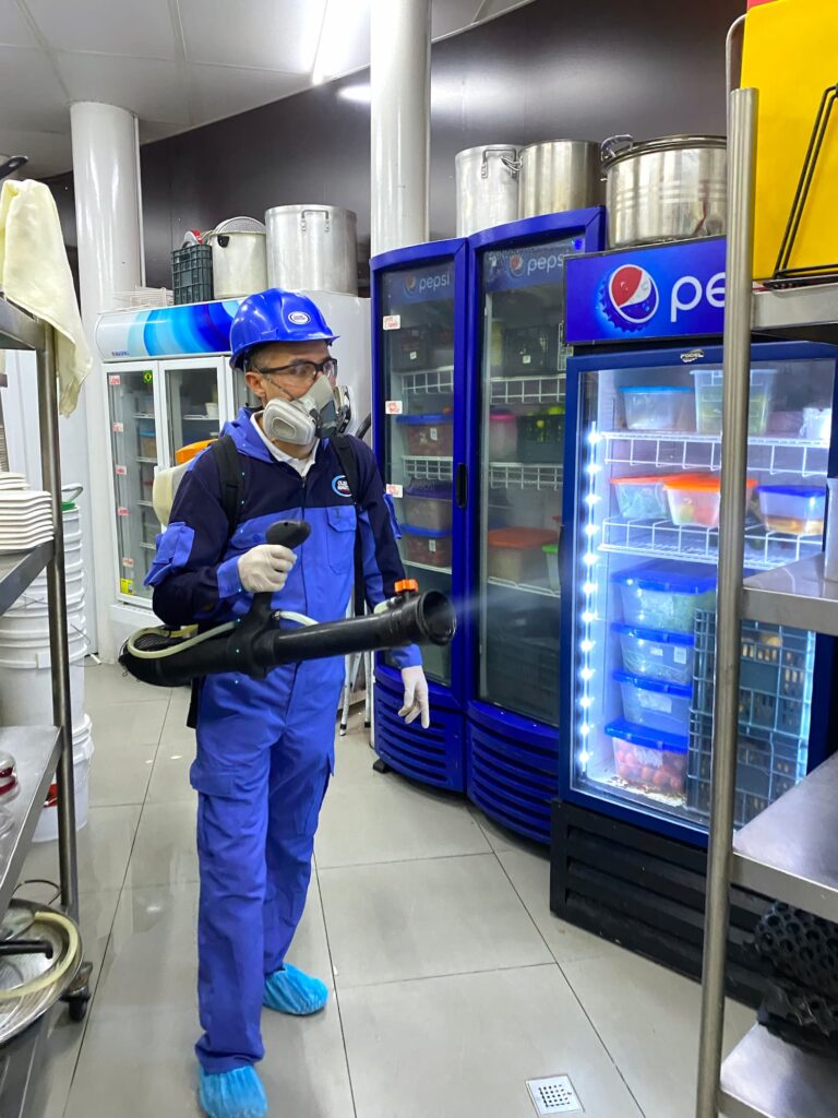 Hombre con traje azul y guantes azules sosteniendo un rociador, realizando fumigación para empresas en Guatemala.