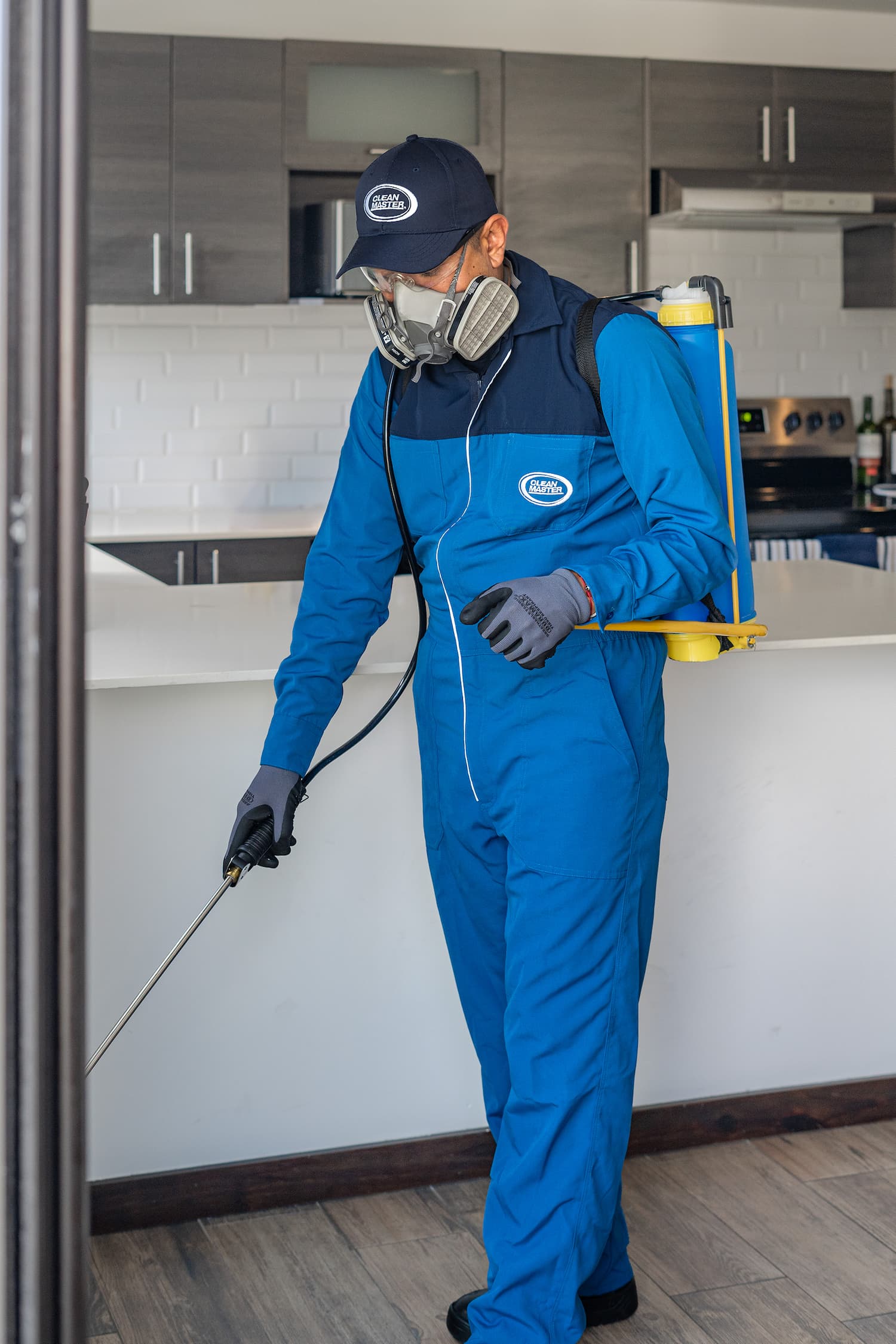 Hombre en overoles azules aplicando fumigación para el control de plagas en una casa en Guatemala.